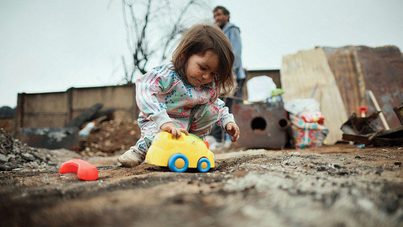 طفلة تلعب بالقرب من منزل عائلتها الذي دمرته الحرائق. رويترز
