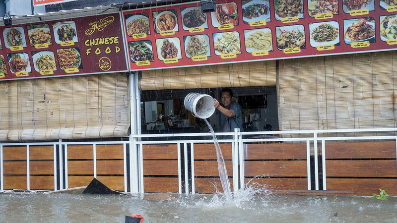 عامل في مطعم بمدينة كوتا يتخلص من مياه الفيضانات بعد دخولها المطعم. إي.بي.إيه