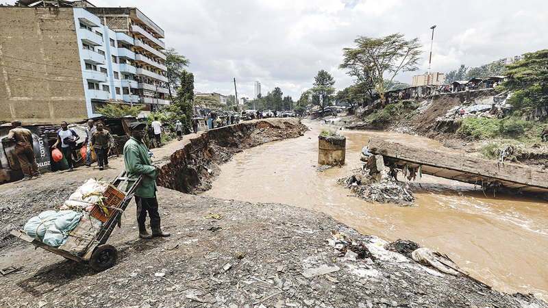 أحد عمال النظافة يقف بجوار جسر مشاة متضرر بعد أن جرفته الفيضانات. إي.بي.إيه