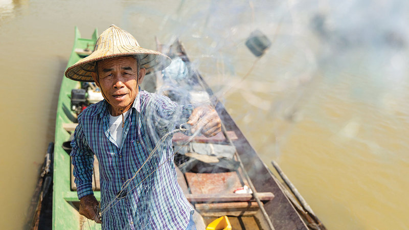 صياد يفك شباكه أثناء رسو قاربه  على ضفاف النهر. أ.ب