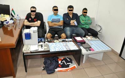 أفراد العصابة وأمامهم البطاقات الائتمانية المزورة والأجهزة المستخدمة في تصنيعها.  من المصدر