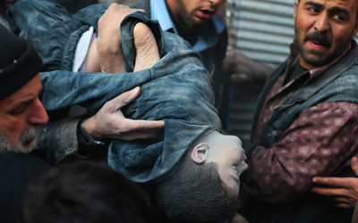 سوريون يحملون جثة طفل قتل بغارة لقوات النظام على دوما.
