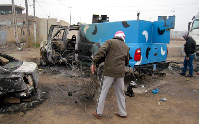 مسلحان من الميليشيات التي سيطرت على الفلوجة بجوار سيارة للشرطة تم إحراقها.رويترز