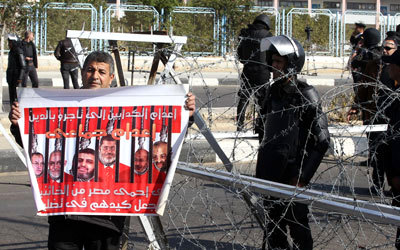 مصري يحمل ملصقاً لقادة من «الإخوان» ضمنهم مرسي  خارج مقر محاكمة الأخير في القاهرة. إي.بي.أيه