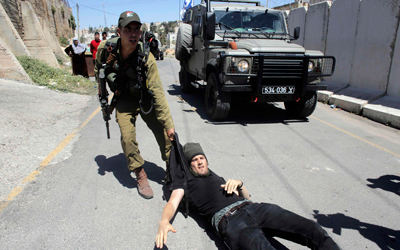 جندي إسرائيلي يسحل ناشطاً أجنبياً خلال اشتباكات بين مستوطنين وفلسطينيين في مدينة الخليل.  رويترز