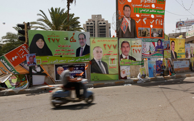 عراقي يسير بدراجته النارية بجوار ملصقات الحملة الانتخابية في ساحة التحرير وسط بغداد. رويترز