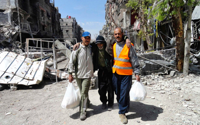 فلسطينيون يساعدون مسناً خلال توزيع المساعدات على مدخل مخيم اليرموك المحاصر في دمشق.  رويترز