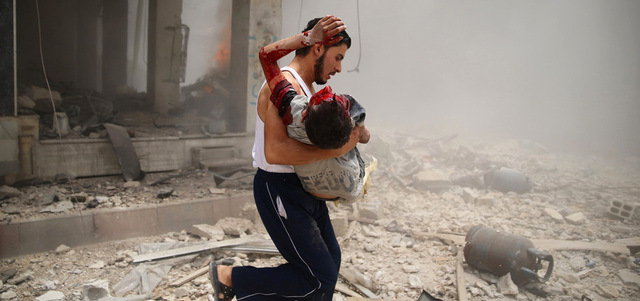 رجل يسعف طفلاً أصيب بانفجار سيارة مفخّخة في سوق مدينة دوما.