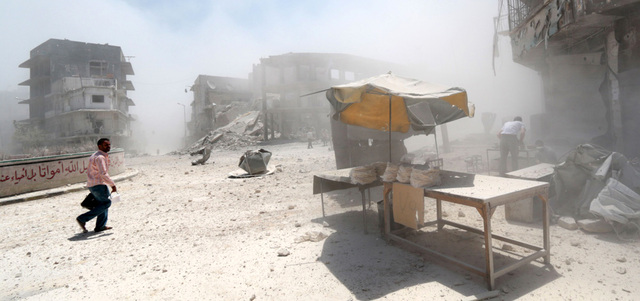 سوريون يمشون وسط الغبار عقب إلقاء قوات النظام برميلاً متفجراً على حي طريق الباب في حلب.  أ.ف.ب