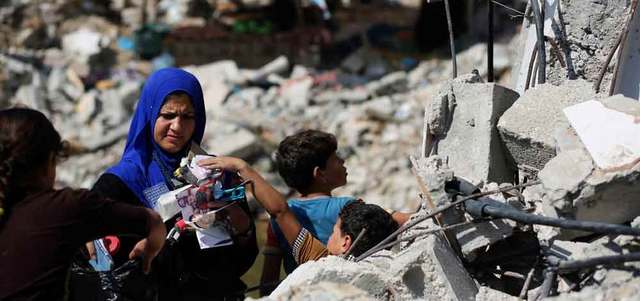 فلسطينية مع أطفالها وسط ركام منزلها في حي الشجاعية الذي دُمر خلال العدوان. إي.بي.إيه