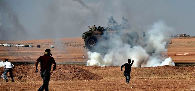 أكراد يرمون الحجارة على مركبة مدرعة تركية تطلق الغاز المسيل للدموع عليهم لإبعادهم عن الحدود مع «عين العرب» قرب بلدة سورج التركية. أ.ف.ب