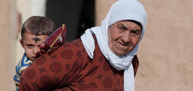مسنّة كردية فرت من مدينة عين العرب السورية تحمل طفلاً على ظهرها في معبر مرشد بينار التركي. أ.ب