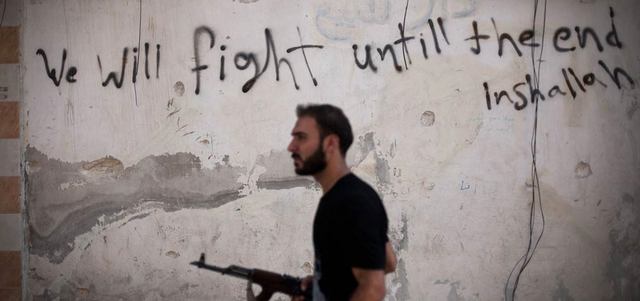 أحد عناصر الثوار في حلب يمر قرب حائط كتب عليه «سنقاتل حتى النهاية». أ.ب
