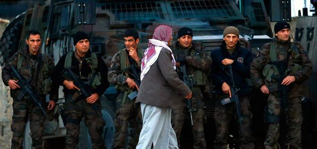 كردي يمر أمام قوات من الشرطة التركية الخاصة تقف خارج بوابة معسكر يستضيف مقاتلي البشمركة في بلدة سروج الحدودية مع سورية.  رويترز