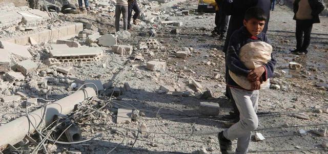 صبي يحمل الخبز وهو يسير أمام أنقاض مبنى دمّر بقصف للقوات النظامية على مدينة الرقة. رويترز