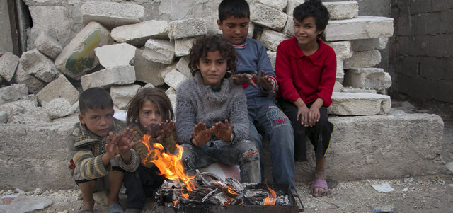 أطفال سوريون يتدفؤون في إحدى المناطق المتضررة من الاشتباكات في أحد أحياء مدينة حلب، أمس. أ.ف.ب