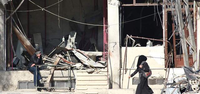 امرأة تسير بأحد شوارع عربين أمام متاجر تضرّرت بقصف القوات السورية للمدينة. أ.ف.ب