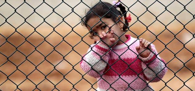 طفلة سورية لاجئة تقف وراء سياج في مخيم أطمة للاجئين قرب الحدود السورية التركية.  رويترز