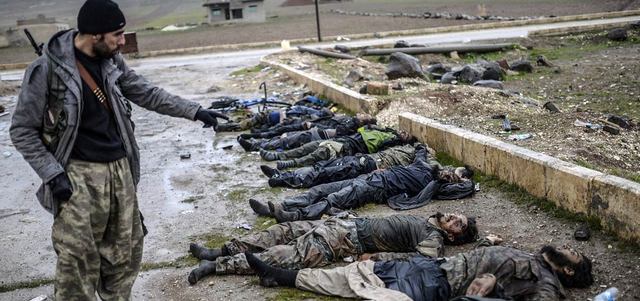 مقاتل كردي يشير إلى قتلى «داعش» في قرية بضواحي عين العرب السورية. أ.ف.ب