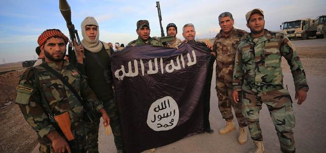 مقاتلون عراقيون موالون للحكومة يحملون علم «داعش» الذي أنزلوه عن خط الجبهة في جلولاء بعد تقدمهم في محافظة ديالى. رويترز