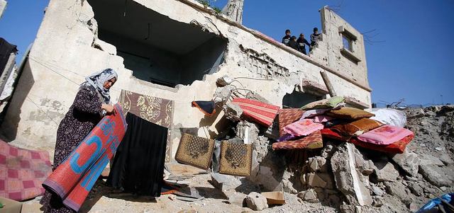 فلسطينية تنشر ملابسها أمام منزلها المدمّر في بيت حانون نتيجة الحرب الإسرائيلية على غزة.  إي.بي.إيه