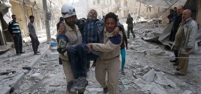عاملا إغاثة يسعفان رجلاً أصيب بإلقاء القوات النظامية برميلاً متفجراً على حي الشعار في حلب.  أ.ف.ب