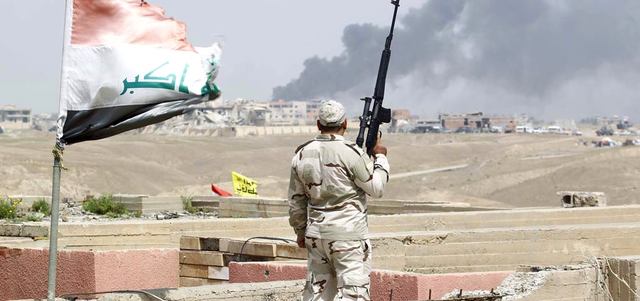 عنصر أمن عراقي يشاهد الدخان المتصاعد جرّاء اشتباكات بين القوات العراقية و«داعش» في تكريت.  رويترز