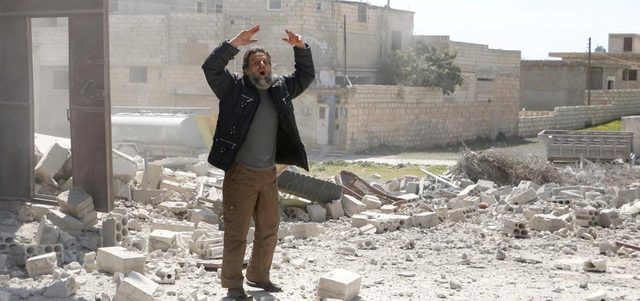 رجل يصرخ لإبعاد أشخاص تجمعوا بموقع استهدفته غارة للقوات النظامية في بلدة سرمين بريف إدلب. رويترز