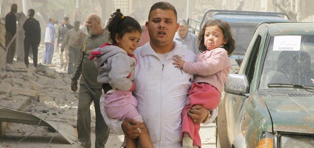رجل يحمل طفلتين ويفرّ مسرعاً من حي الثورة بمدينة إدلب بعد أن قصفته القوات النظامية ببرميل متفجر.  رويترز