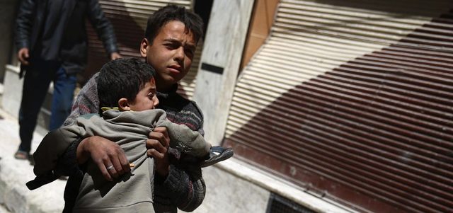 صبي سوري يحمل طفلاً أصيب بغارة للقوات النظامية على مدينة دوما بريف دمشق. أ.ف.ب