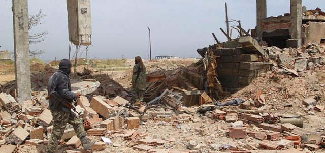 مقاتلان من «جيش الفتح» يمشيان أمام مستودع للذخيرة داخل معسكر القرميد في ريف إدلب بعد السيطرة عليه.  رويترز