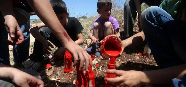 مجموعة من الصبية الفلسطينيين يعبئون زجاجات بلون الدم خلال المواجهات مع الاحتلال في كفر قدوم. أ.ف.ب