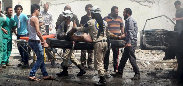 عناصر من الدفاع المدني يحملون جثة متفحمة لأحد القتلى ببرميل متفجر ألقته القوات النظامية على  محطة للحافلات في منطقة جسر الحج بحلب.  رويترز