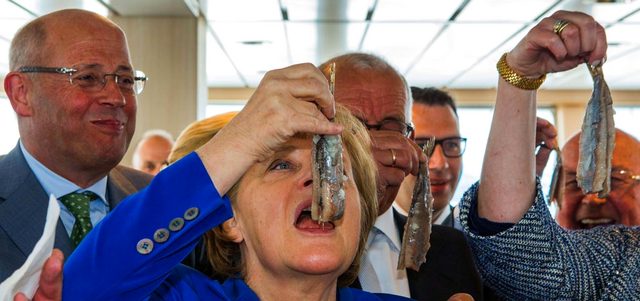 ميركل تأكل مخلل السمك في احتفال بتدشين أحد قوارب الصيد. د.ب.أ