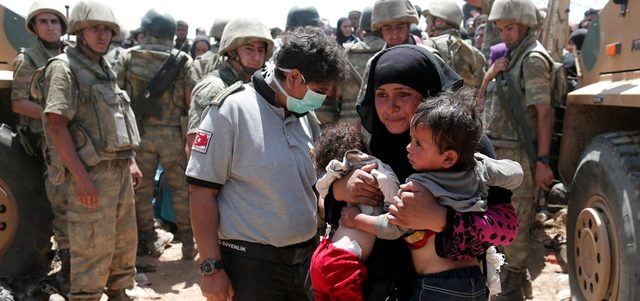 لاجئة سورية تحمل طفليها على الجانب السوري من معبر أكتشاكاليه الحدودي في محافظة شانلي أورفا جنوب شرق تركيا.  إي.بي.إيه