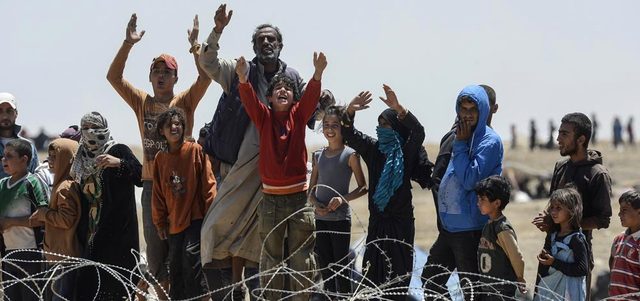 سوريون فروا من المواجهات بين الأكراد و«داعش»، يقفون عند الحدود التركية السورية قرب بلدة تل أبيض. أ.ف.ب