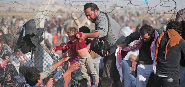 لاجئون سوريون يساعدون طفلاً على عبور السياج الحدودي في تل أبيض قرب معبر أقجة قلعة التركي.  أ.ب