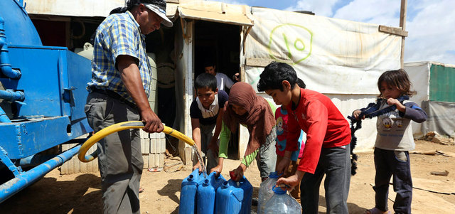 سوري يملأ غالونات المياه لأطفال بمخيم للاجئين في بلدة فاعور بالبقاع اللبناني. أ.ب