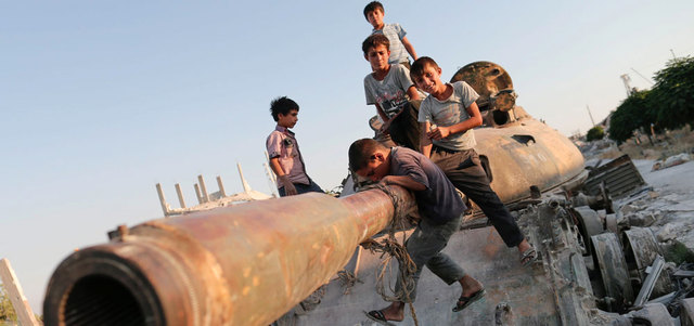 أطفال سوريون يلعبون على بقايا دبابة دمرت خلال المواجهات بين الأكراد وتنظيم «داعش» جنوب مدينة عين العرب (كوباني). أي.بي.إيه