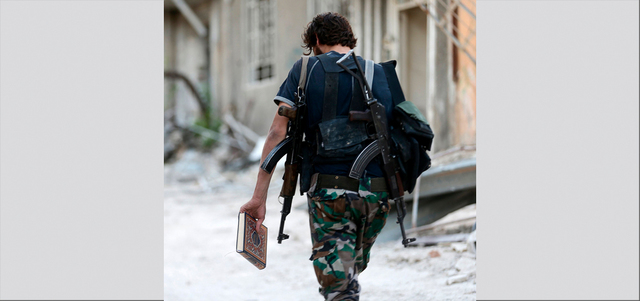 مقاتل من الجيش السوري الحر يحمل بيده القرآن الكريم ويمشي في أحد شوارع حي جوبر بضواحي دمشق.  رويترز