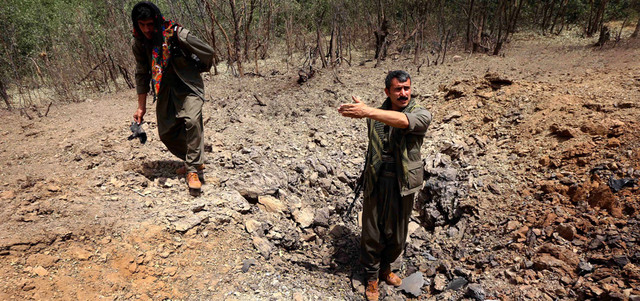 مقاتلان من حزب العمال الكردستاني يتفحصان حفرة أحدثتها قنابل أسقطها الطائرات التركية. أ.ف.ب