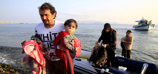 مهاجر سوري يحمل طفلته لدى وصوله على زورق إلى شاطئ في جزيرة كوس اليونانية. رويترز