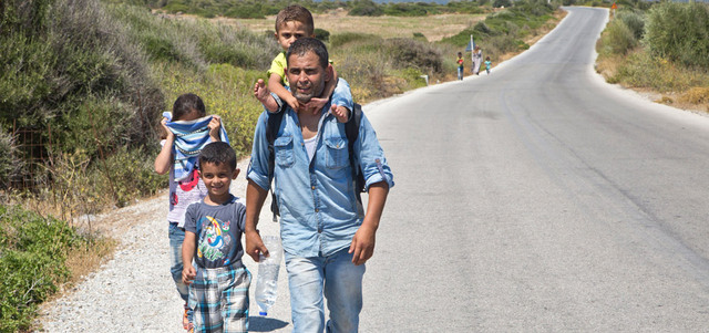 مهاجر سوري من مدينة الرقة يحمل ابنه على ظهره في طريقه سيراً على الأقدام لمسافة 60 كيلو متراً من مدينة سكالا سيكامينا إلى بلدة ميتيليني في اليونان. أ.ب