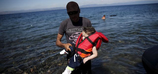 لاجئ سوري يحمل طفلاً عقب وصولهما إلى الشواطئ اليونانية. رويترز