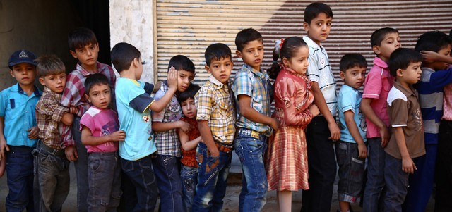 أطفال سوريون فقدوا أحد والديهم أو كليهما يصطفون لحضور حفل في مدينة دوما المحاصرة بريف دمشق. أ.ف.ب