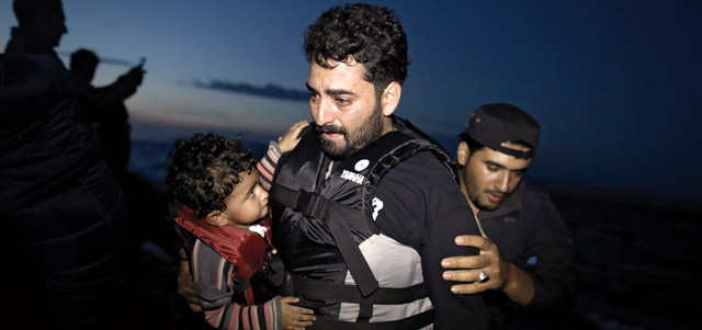 لاجئ سوري يبكي وهو يحتضن طفله لدى نزوله من قارب مطاطي في جزيرة ليسبوس اليونانية. إي.بي.إيه