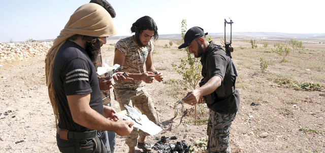 مقاتلون من حركة «أحرار الشام» يجمعون حطام طائرة مجهولة من دون طيار تحطمت في ريف إدلب.   رويترز