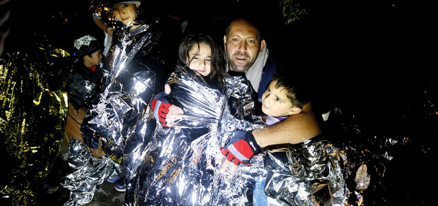 لاجئ سوري يحاول إبقاء أطفاله دافئين بعد إنقاذهم في جزيرة ليسبوس اليونانية. رويترز