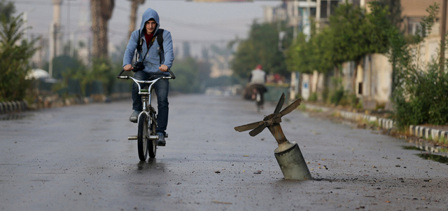 شاب يركب دراجته بالقرب من قذيفة لم تنفجر أطلقتها القوات النظامية على مدينة دوما بريف دمشق.  رويترز