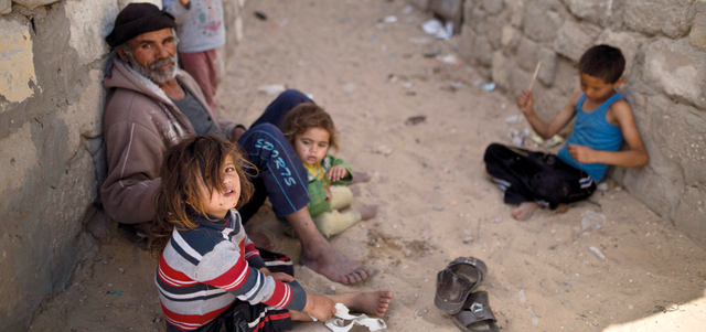 أفراد من عائلة فلسطينية يجلسون في الظل بمنطقة فقيرة بخانيونس جنوب غزة. أ.ف.ب